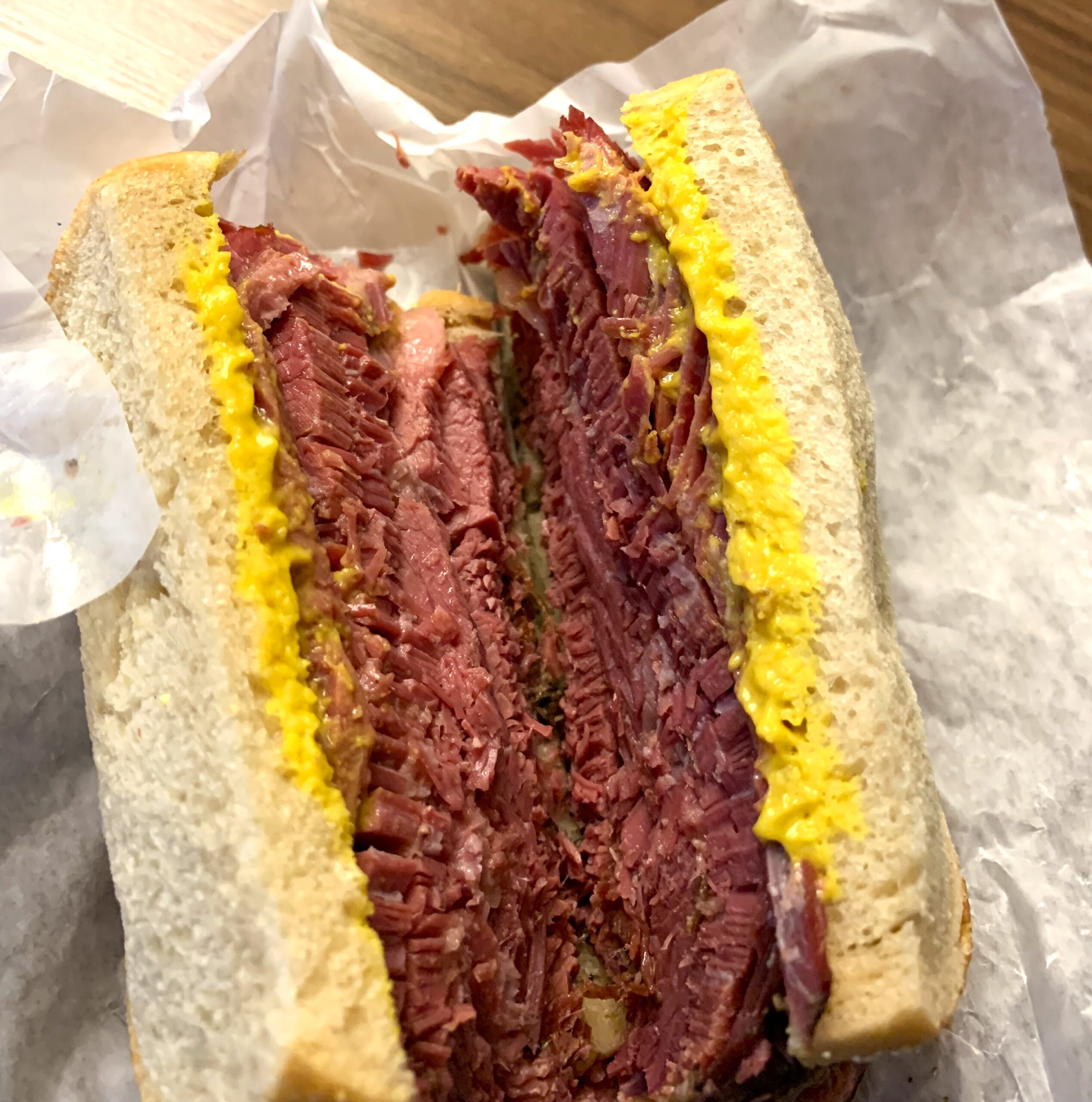 Sandwich packed with several layers of sliced brisket on bread covered in yellow mustard.