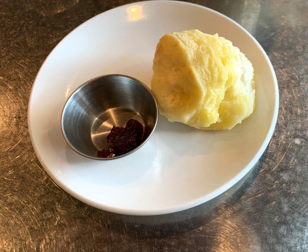 A plate with a small puffy biscuit and a small ramekin with blood orange jam.