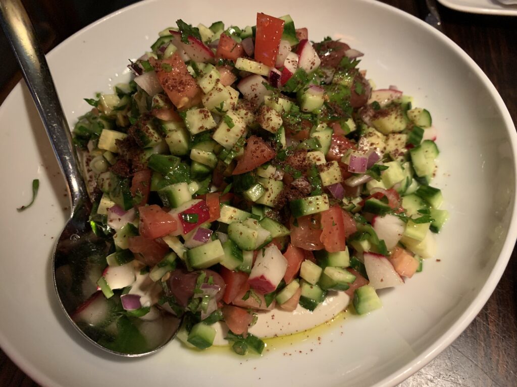 Plate of Israeli salad - mix of cucumbers, tomatoes, red onions, sumac, fresh herbs.