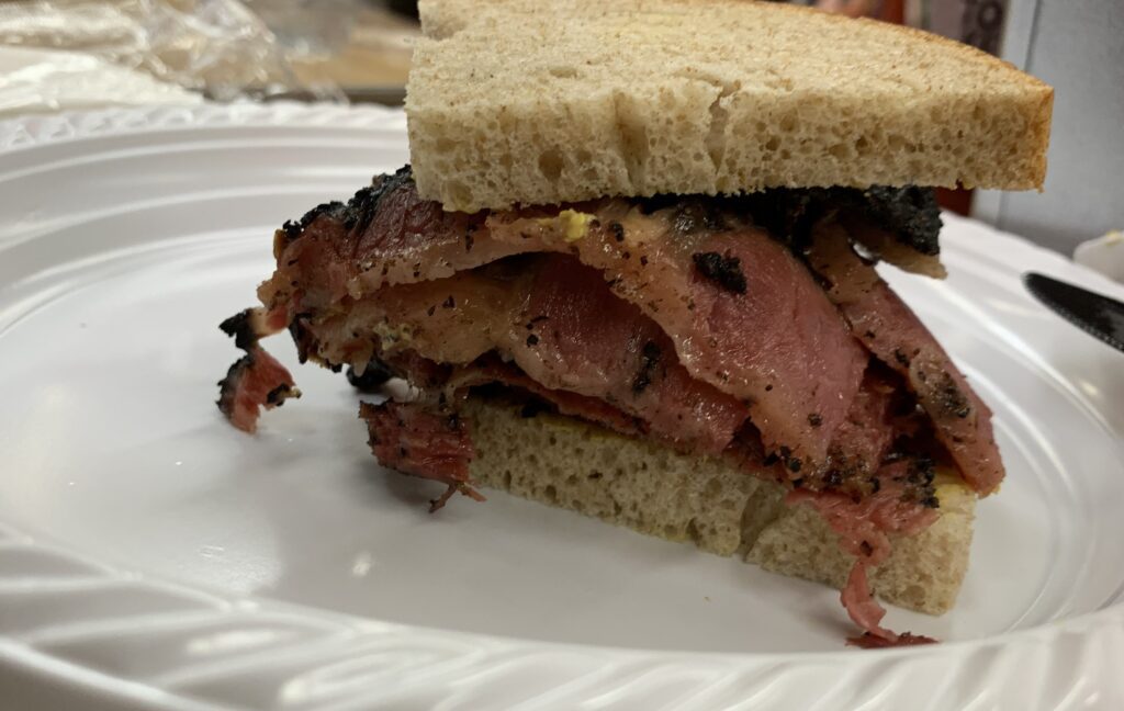 A moist-appearing pastrami on rye sandwich with mustard.
