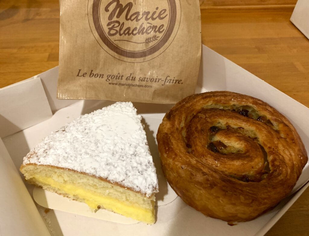 A box containing pastries, a custard-filled cake slice dusted with powdered sugar and a rolled pastry filled with dried fruit.