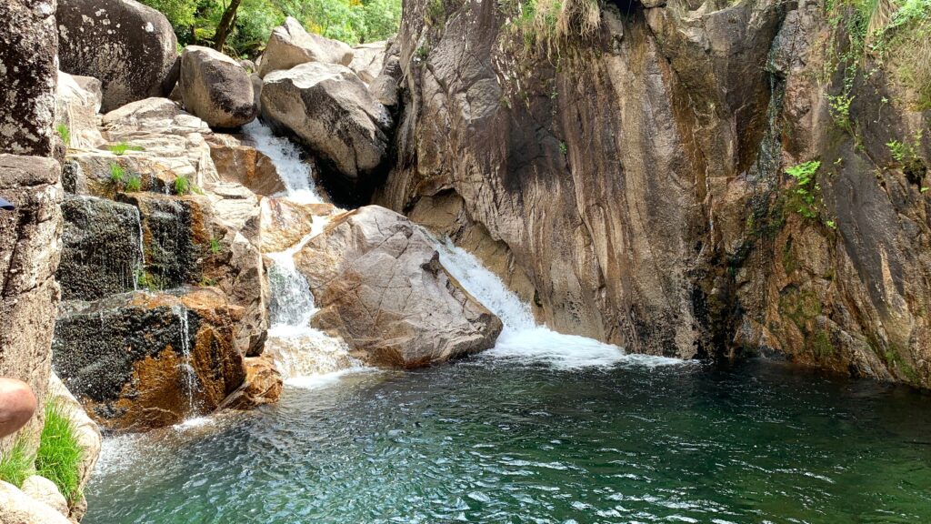 Water cascades over some rocks into a clear green/blue pool.