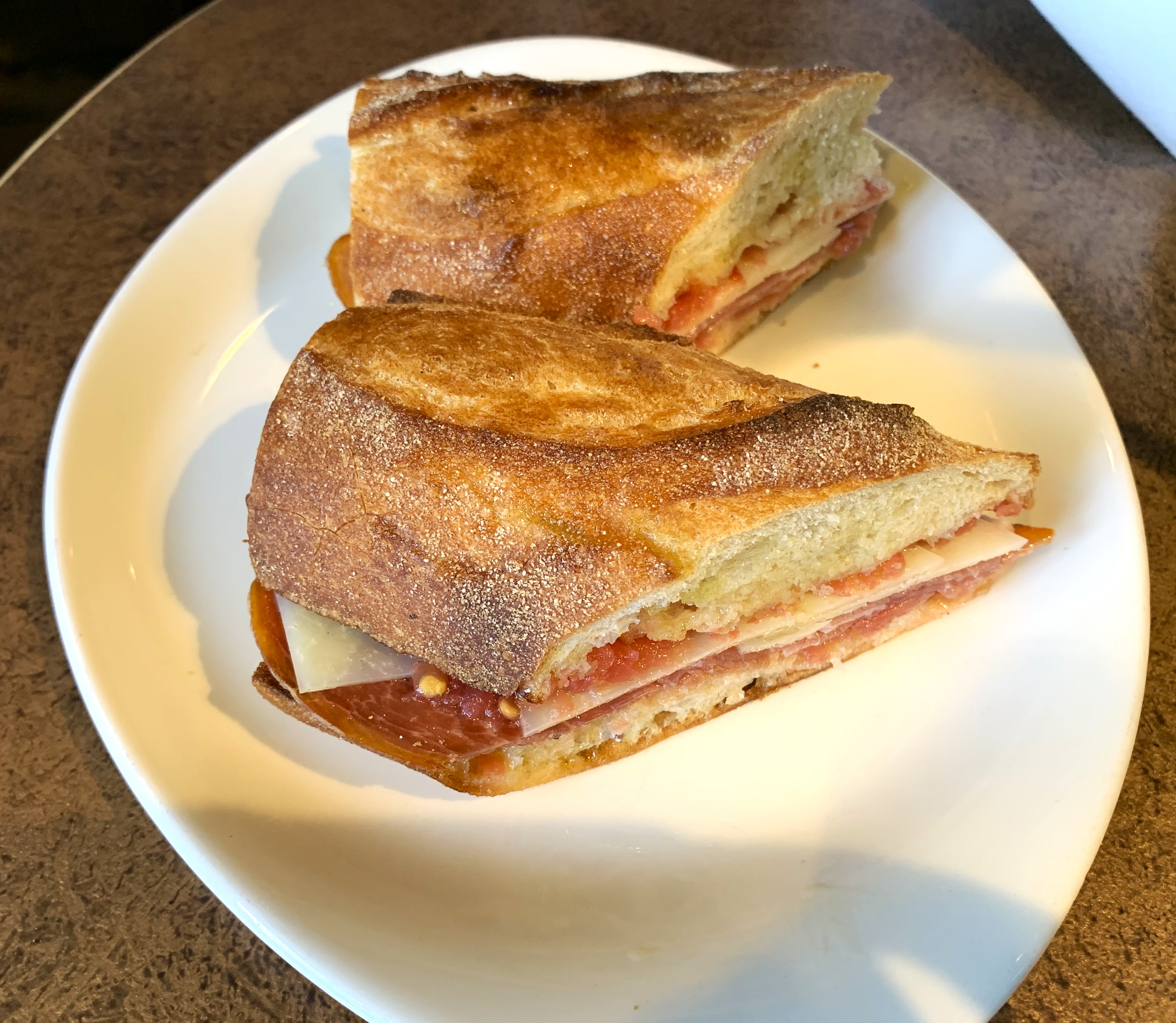 Sandwich on a crusty roll cut in two containing jamon, tomate fresco and Manchego cheese