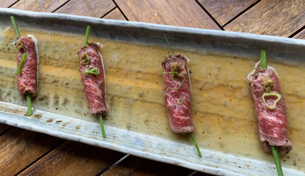 Four thinly sliced rolled Waygu Beef with spring onion spear in a clear tannish broth.