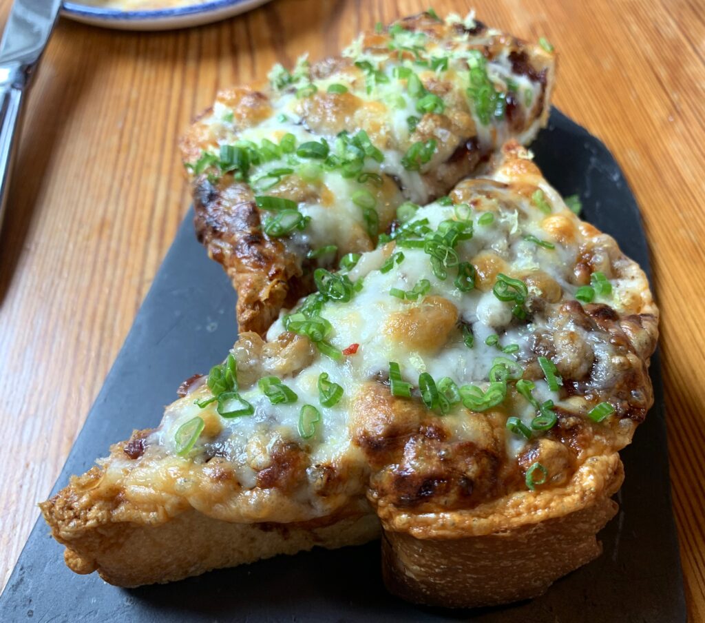 Two open-faced pieces of toasted topped with bone marrow, cheese and green onions.