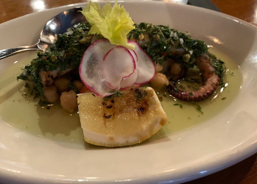 Grilled octopus served atop chickpeas, finished with oil and topped with chimichurri.