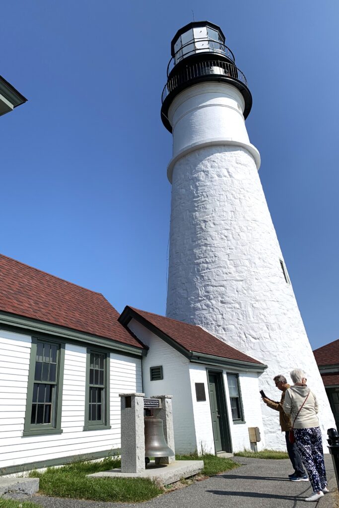 White lighthouse with a large bell in the foreground.