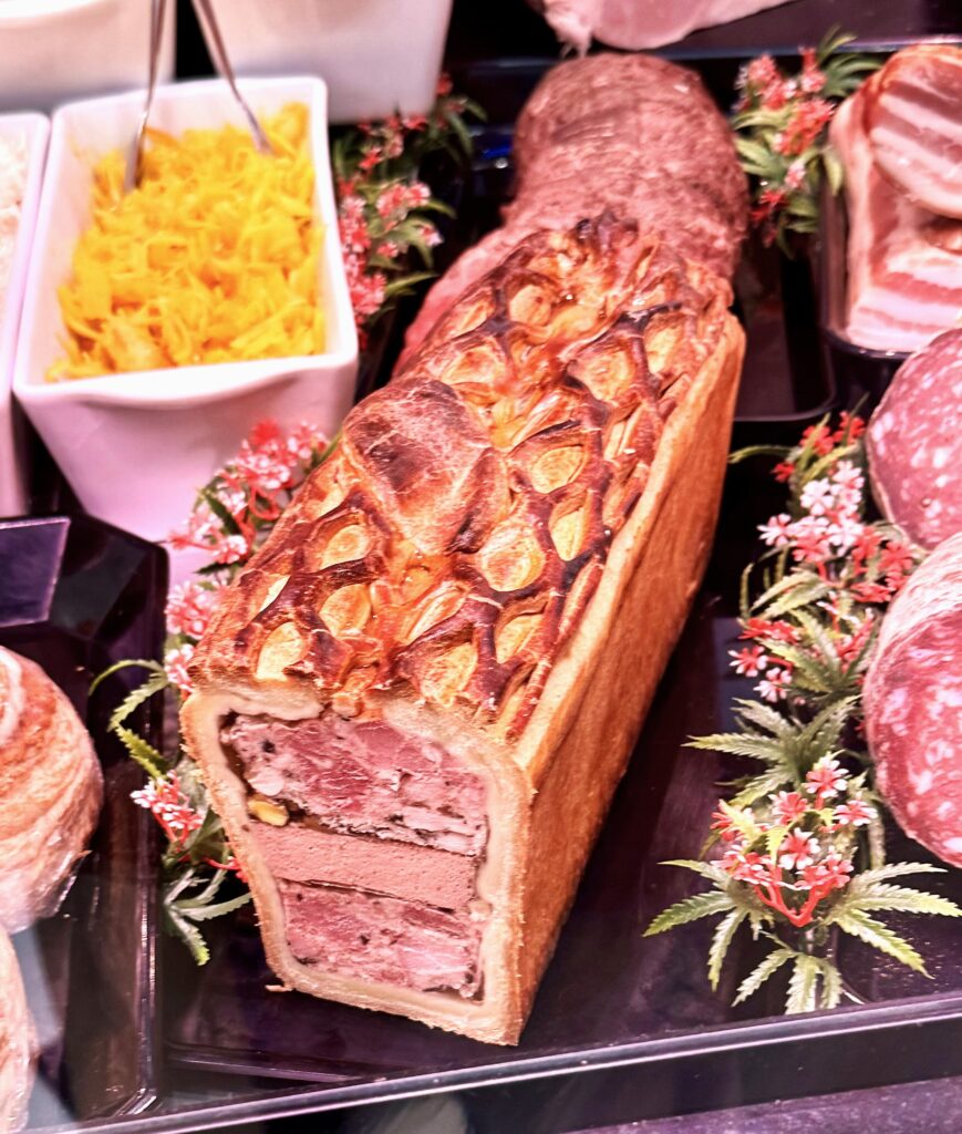A Glass case with pate en croute a long loaf of pastry containing a triple of pate sandwiched by jellied pork.