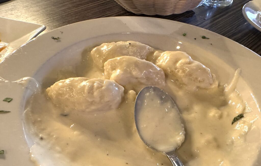 A plate of 4 pieces of gnocchi in a white sauce with a spoon on the side.