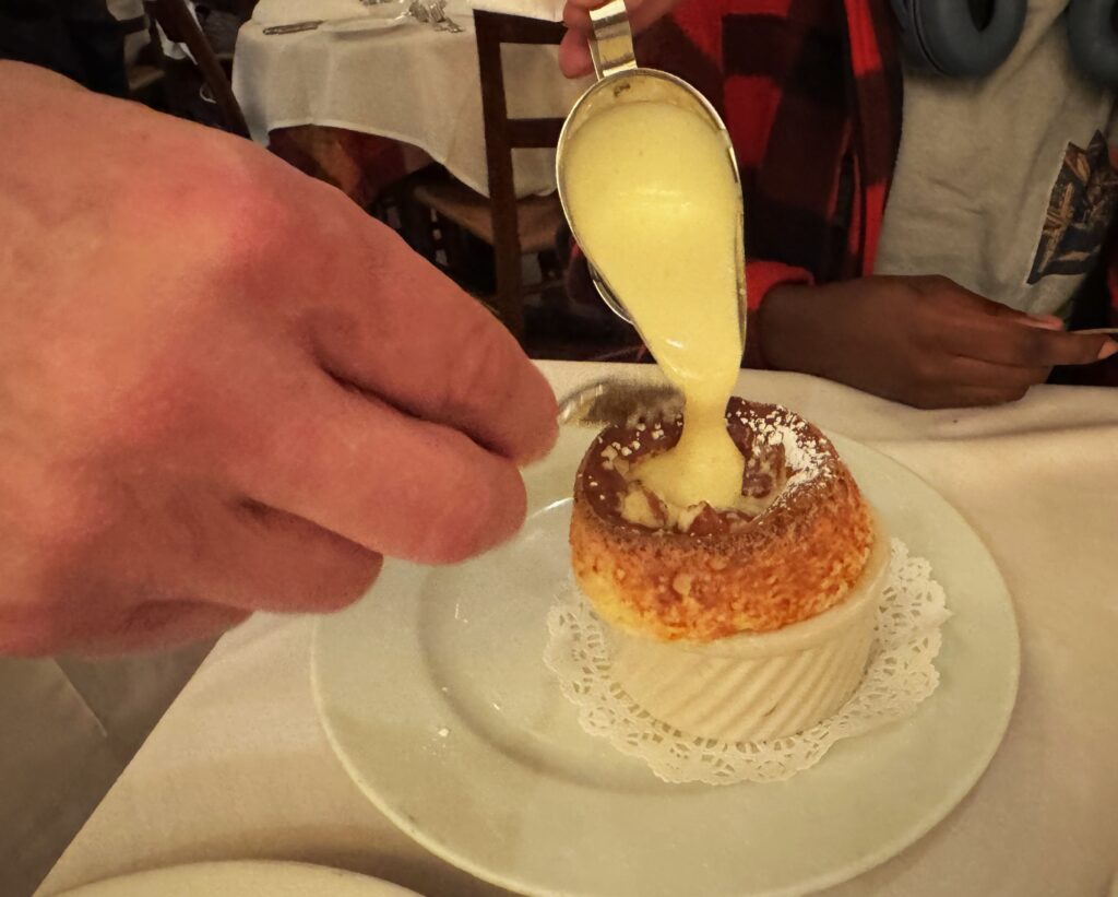 A hand pouring a custard into the broken top of a Grand Marnier souffle.