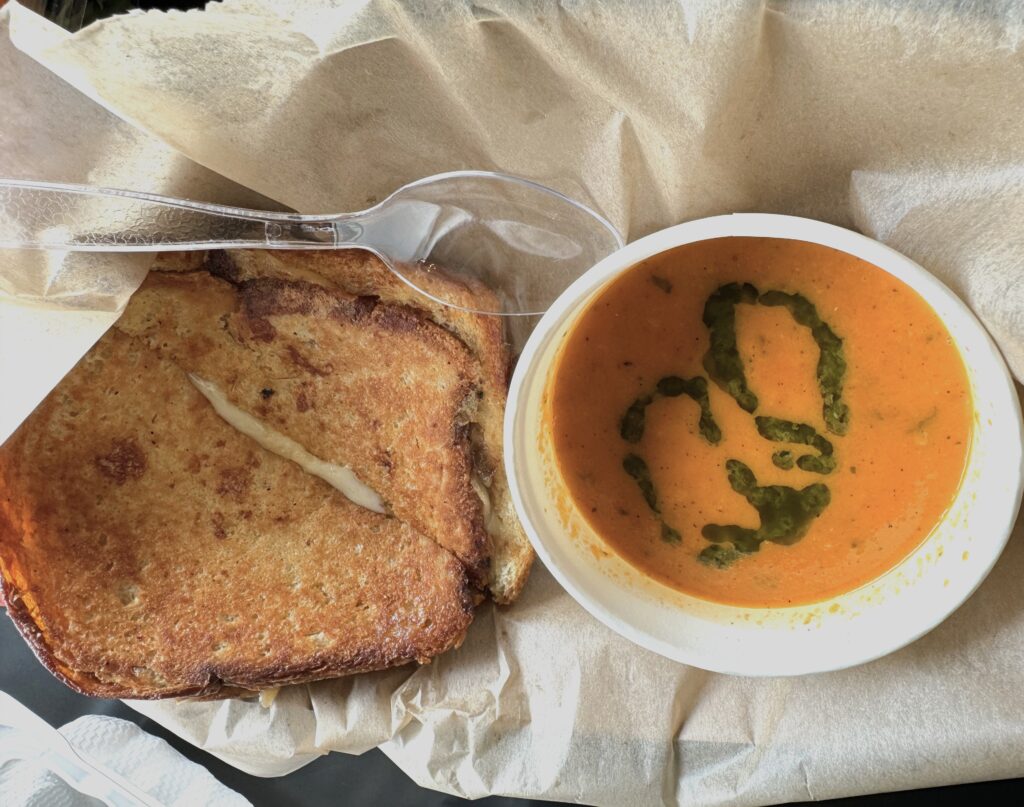 A small bowl of tomato soup with green herb swirls, and a grilled cheese sandwich cut in half.