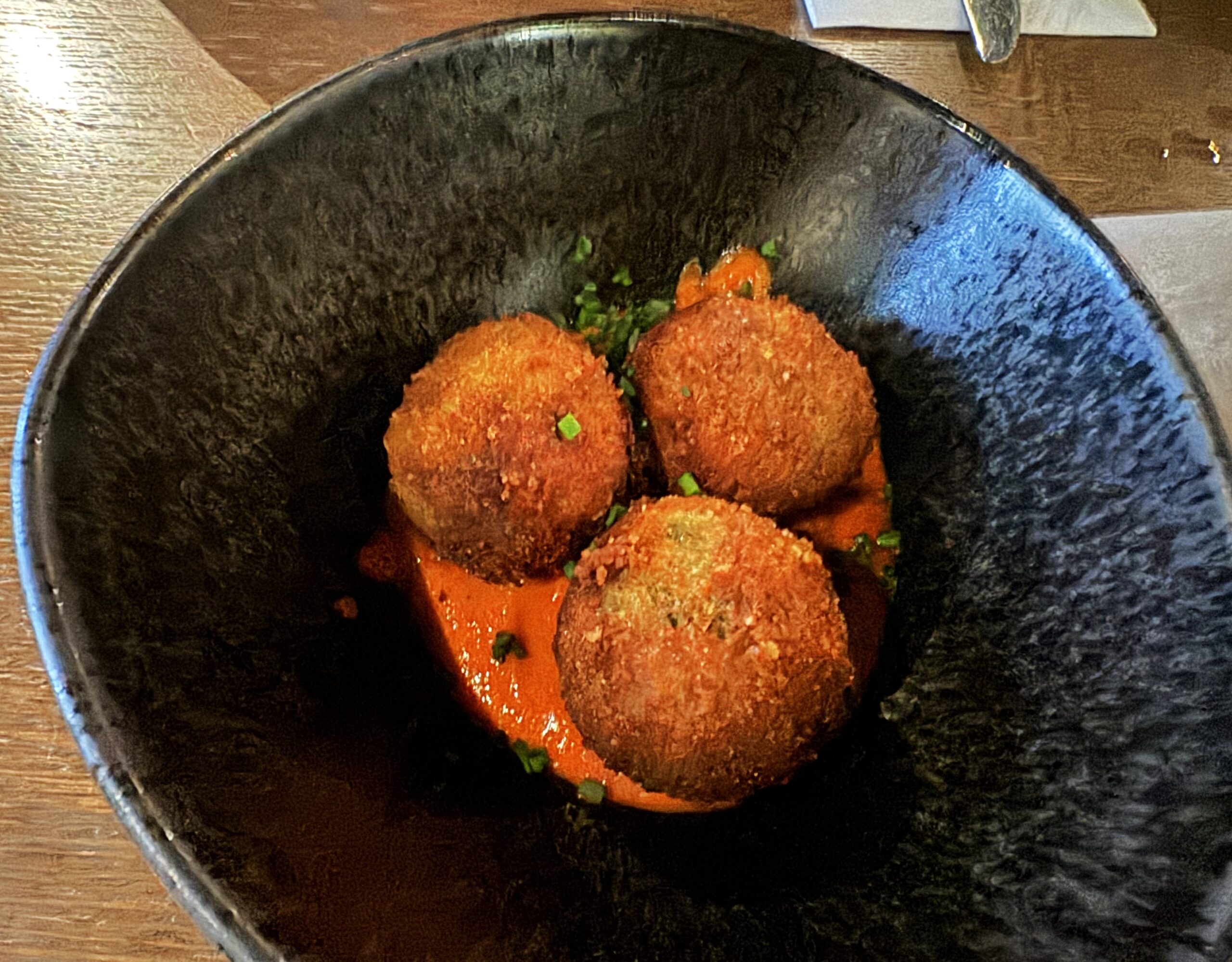Three round, fried golden, brown-colored balls in a red sauce garnished with chives.