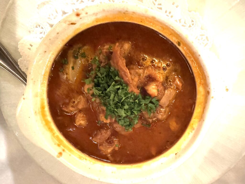 Bowl filled with pieces of Tripes (tripe) stew with potatoes and carrots topped with green herbs.